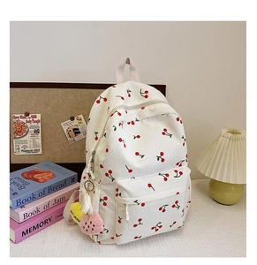 White corduroy backpack with red cherry print on a desk with a pleated lamp