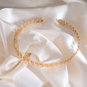 Vue détaillée du collier doré ondulé tissé sur fond de soie élégante et de plâtre