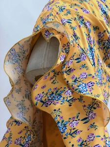 Detail of yellow floral dress showing ruffle layers and chiffon fabric on a mannequin