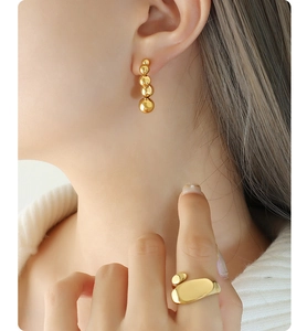 Close-up of minimalist golden bead earrings and irregular organic ring on a model