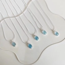 Detail of five S925 silver necklaces featuring light blue oval heart pendants on beige background
