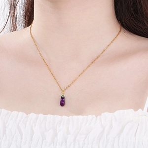 Macro detail of a purple eggplant pendant on a dainty gold chain worn on the neck