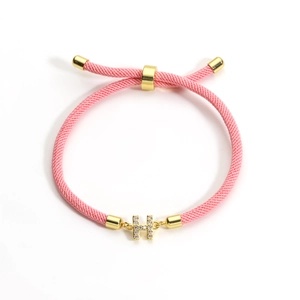 Macro detail of pink braided rope bracelet featuring a gold H-shaped charm with zircons