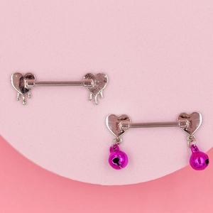 Dettaglio di piercing capezzolo a cuore argentato con campanelli e smalto rosa
