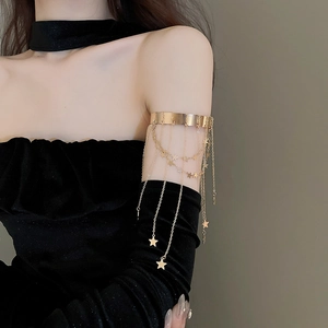Detailed view of golden metal arm cuff featuring hanging star tassels on a model arm