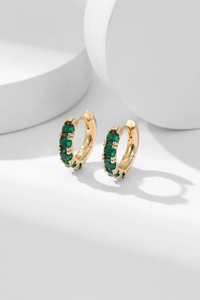 Detailed shot of gold plated earrings featuring five prong-set green cubic zirconia stones