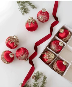 Close-up of red velvet Christmas balls with gold glitter and pearl details in a white gift box