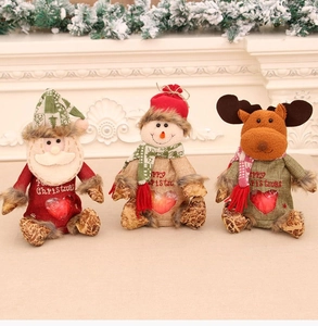 Three Christmas gift bags with Santa, Snowman, and Reindeer dolls on a festive fireplace