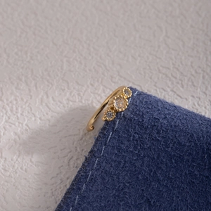 Macro shot of gold-plated leaf-style nose ring with three clear zircons on denim