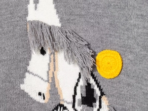 Detail of horse embroidery with grey 3D fringe and yellow sun on a knitted sweater
