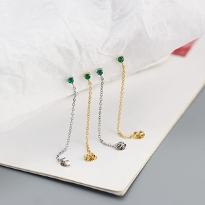 Macro shot of silver and gold chain earrings with green stones on a white texture