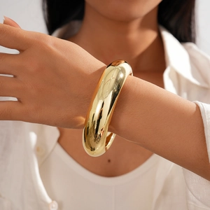 Polished chunky gold minimalist bangle bracelet worn on a woman wrist detail view