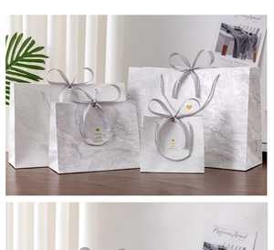 Multiple sizes of marble pattern gift bags with grey ribbon bows on a wooden table