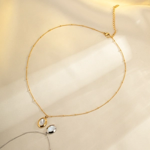 Gold and silver stainless steel oval shell pendant necklaces on silk fabric background
