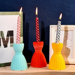 Three colorful striped hourglass candle holders with spiral candles lit on a wooden shelf
