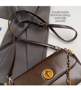 Detail of dark brown leather crossbody bag featuring gold chain and turn-lock closure