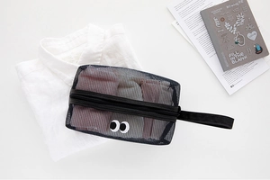Close-up of black mesh cosmetic bag with big eyes pattern and side handle on desk