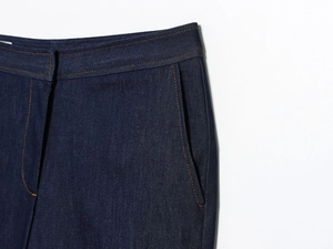 Détail d'un pantalon en denim indigo foncé avec taille haute et surpiqûres orange contrastées