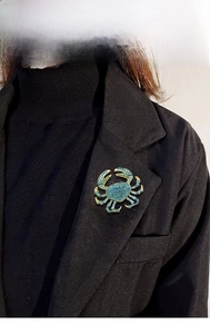 Detailed view of a gold alloy crab brooch with blue rhinestones on a black blazer