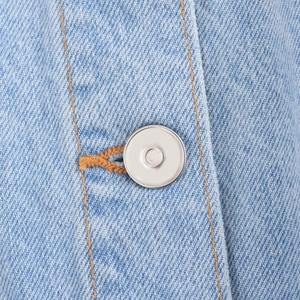 Close-up of light blue denim fabric with silver metal button and orange contrast stitching