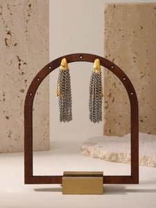 Detail von zweifarbigen Gold- und Silberketten-Ohrringen an einem dunklen Holzständer