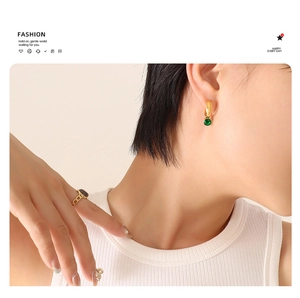 Close-up of elegant gold earrings with green gems and a black stone chain ring worn by a model