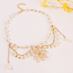 Detail of gold floral pendant with faux pearl tassels on a minimalist body chain