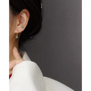 Close-up of elegant gold clover earrings with green gemstones worn by a model