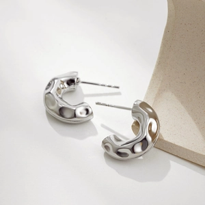 Detailed close-up of C-shaped silver earrings with textured hammered metal finish