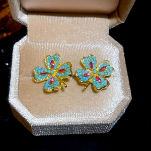 Close-up of gold-plated clover earrings with blue and deep red gemstones in velvet box