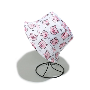 Detailed view of white bucket hat with cute pink pig pattern on a black stand