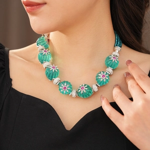 Detail of vintage floral necklace with emerald green petals and pink gemstone core