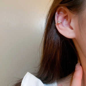 Detailed view of a gold-plated bow-shaped ear cuff with sparkling zircons on model ear