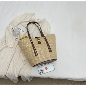 Detail of woven straw tote with brown leather straps and metal buckle on white fabric