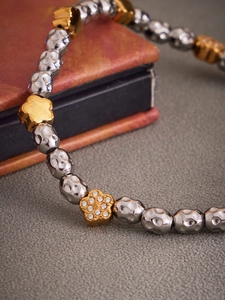 Macro shot of stainless steel hammer-textured beads and zircon flower charm on elastic bracelet