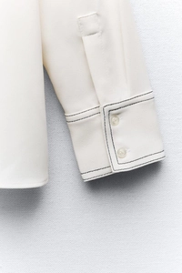 Macro detail of ivory white shirt sleeve with black contrast stitching and dual buttons