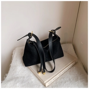 Detail of black suede handbag featuring gold zipper and leather strap on white plush background