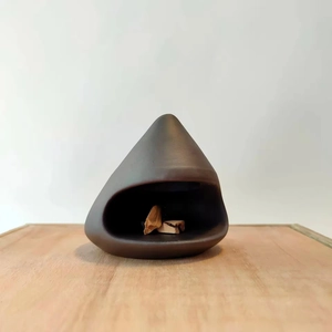 Macro detail of a dark brown ceramic Palo Santo holder on a minimalist wooden surface