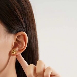 Detail of a gold clover earring with twisted texture and centered zircon on a model ear