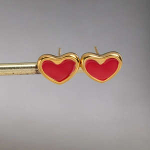 Vue détaillée de boucles d'oreilles cœur dorées avec émail rouge sur un support