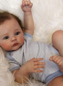 Close-up of lifelike Meadow reborn doll with 3D skin, blue eyes, and striped romper