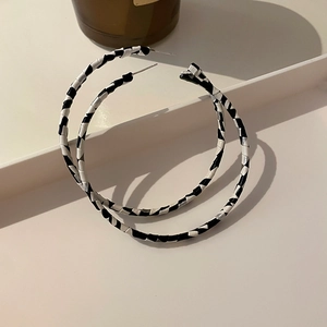 Close-up of geometric hoop earrings with black and white leather woven texture design