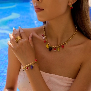 Close-up of gold jewelry set with colorful fruit charms against blue pool background