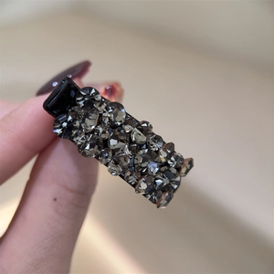 Détail d'une pince à cheveux noire en métal avec strass gris et design rectangulaire