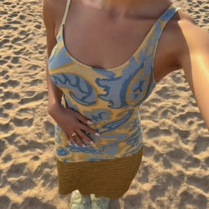 Sleeveless knitted dress with abstract yellow and blue print on sandy beach background