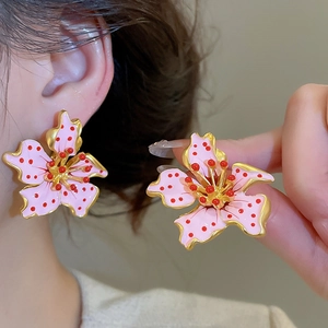 Detail view of pink enamel flower earrings with golden edges and red floral centers