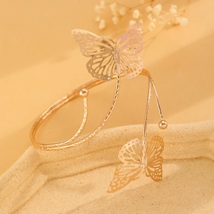 Detail of a gold butterfly arm cuff with hollow wings on a textured beige tray