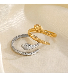 Close-up of gold and silver snake rings with textured scales on beige silk fabric