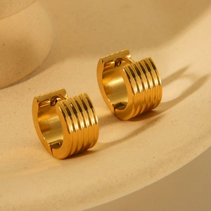 Macro detail of gold chunky hoop earrings with vertical ribbed texture on a ceramic tray