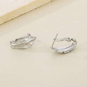 Close-up of silver leaf-shaped stud earrings with fine texture on beige background